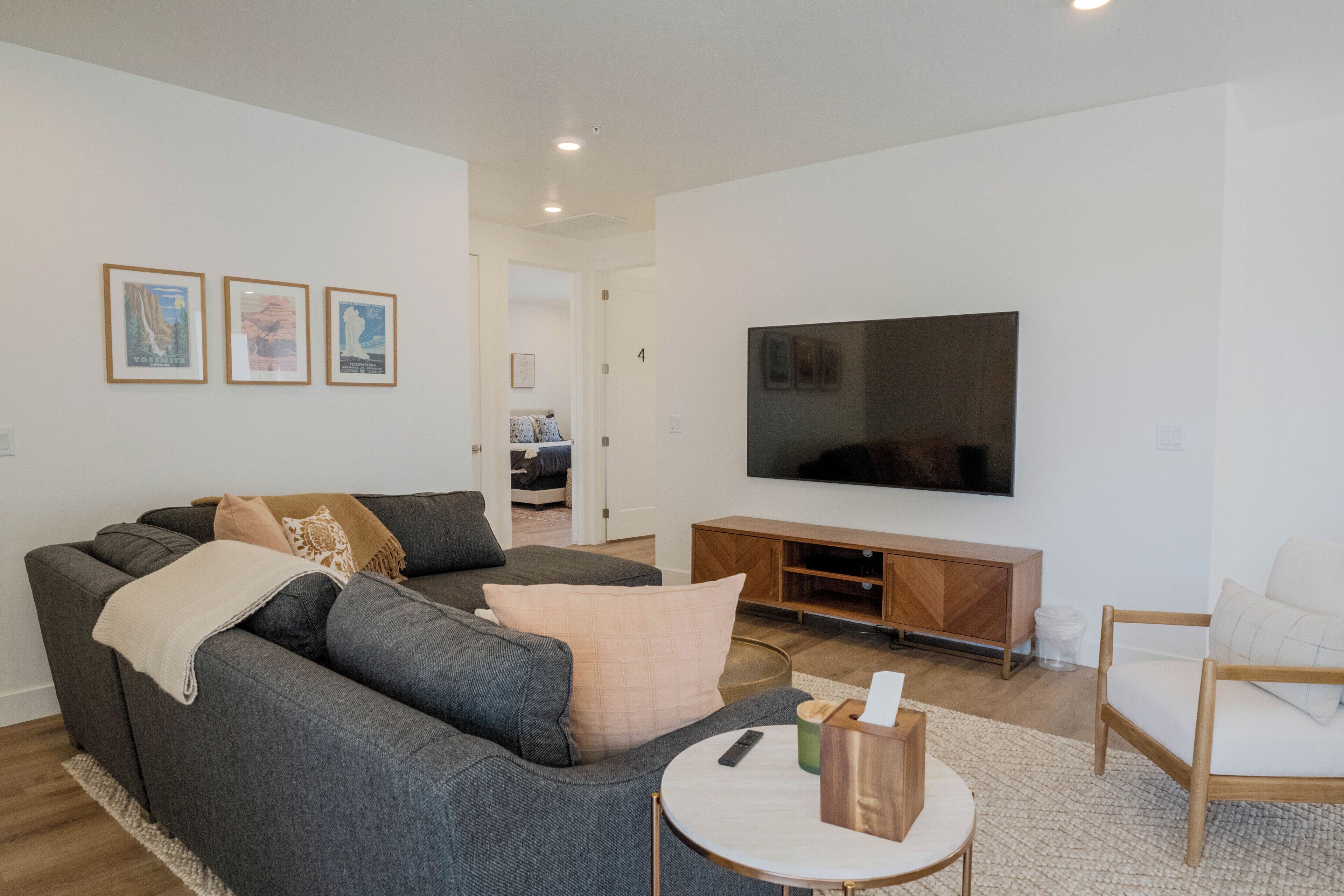 Ein modernes Wohnzimmer mit einem grauen Sofa, einem Holz-TV-Schrank und einem Flachbildfernseher.