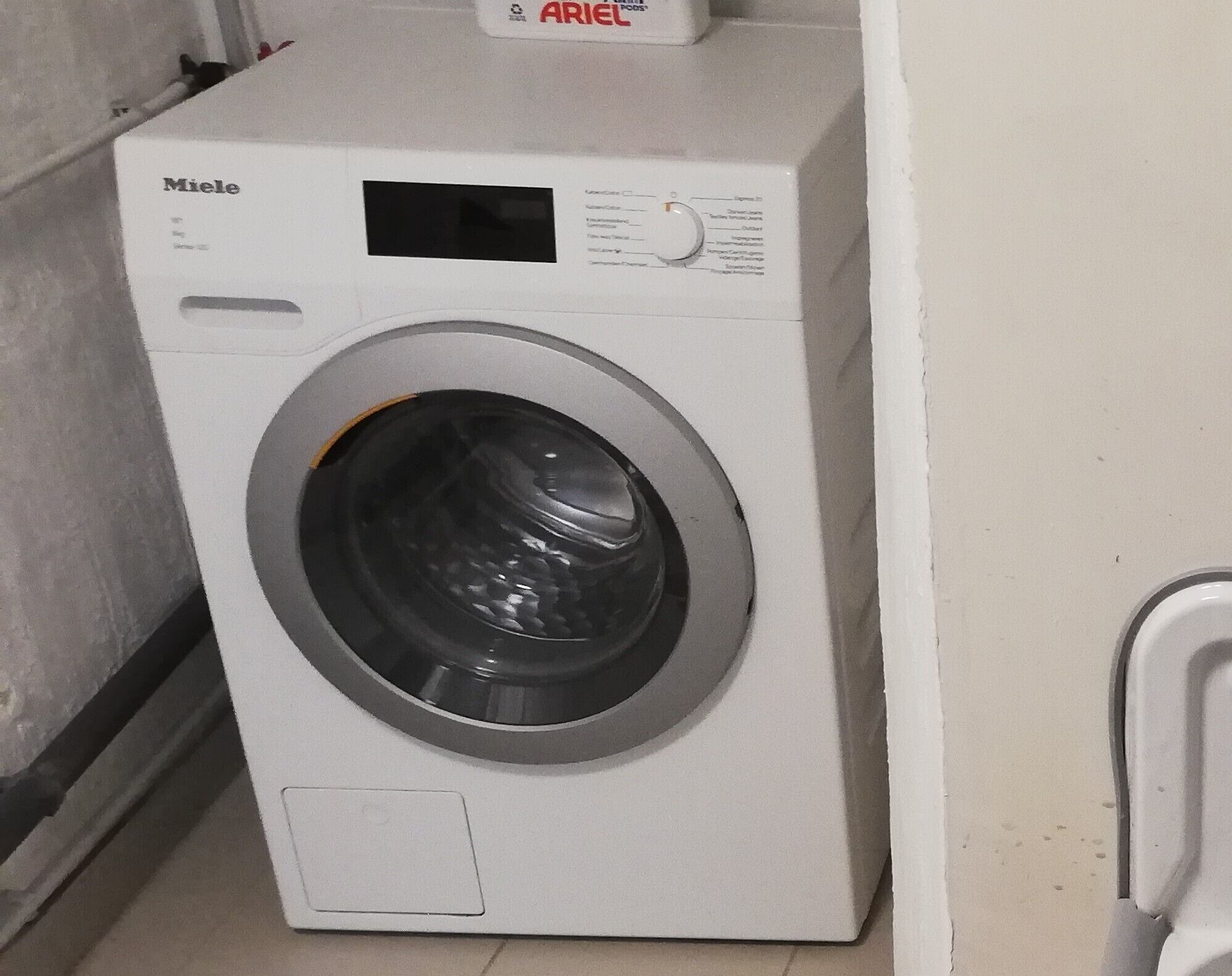 Une machine à laver Miele blanche, dotée d’un panneau de commande et d’une porte à chargement frontal.