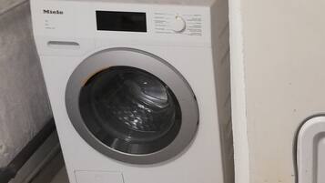 Une machine à laver Miele blanche, dotée d’un panneau de commande et d’une porte à chargement frontal.