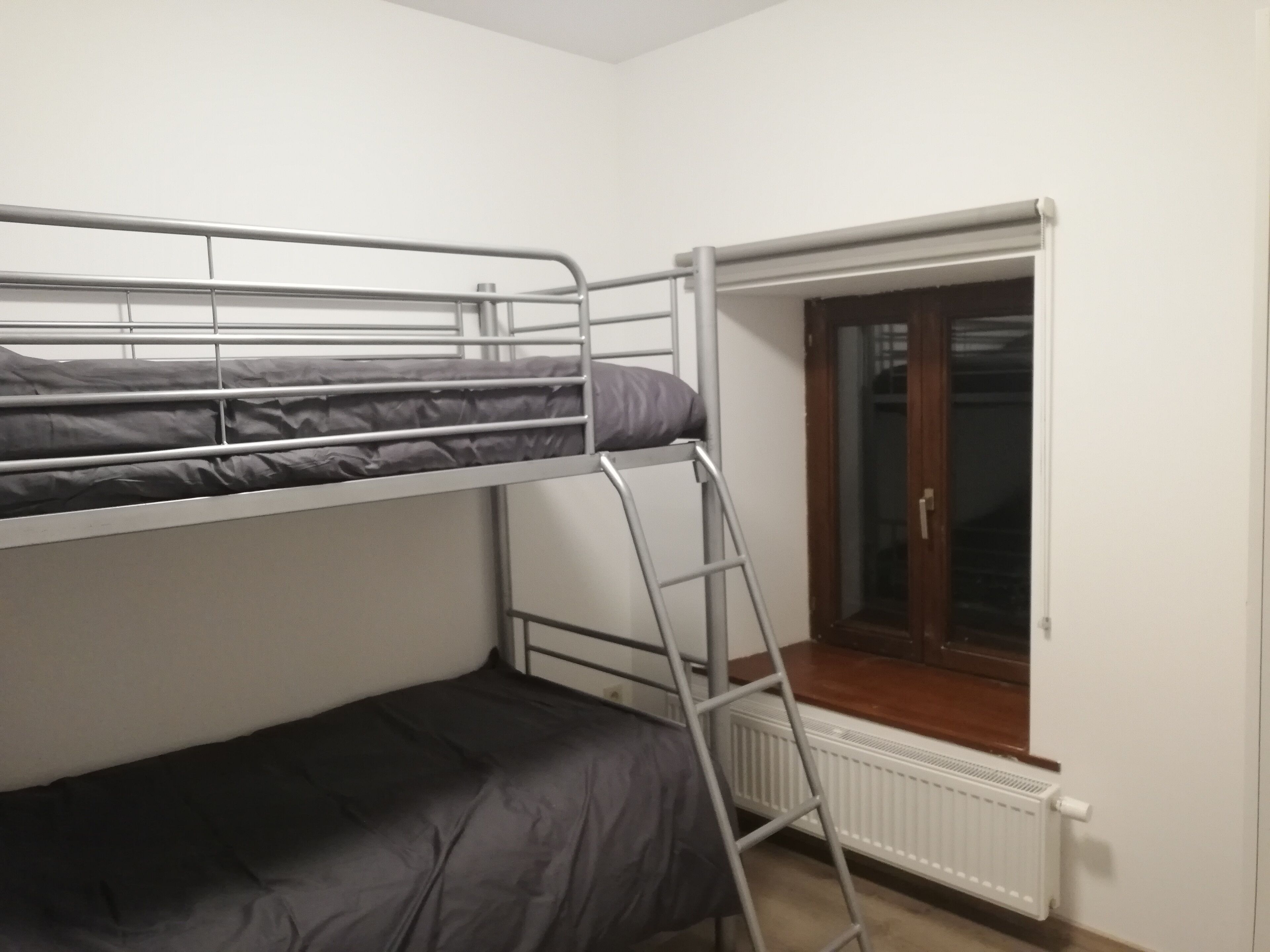 Een slaapkamer met een stapelbed, een raam en een radiator.