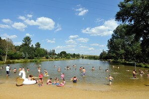 Un espace de baignade extĂ©rieur trĂšs frĂ©quentĂ©, oĂč les gens profitent de lâeau, entourĂ© dâarbres et sous un ciel dĂ©gagĂ©.