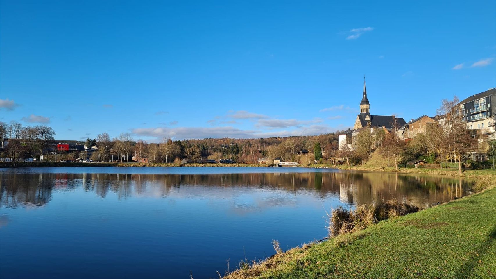 A calm lake with a church and residential buildings in the background.