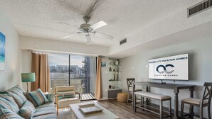 Ein geräumiges Wohnzimmer mit Sofa, Couchtisch und Essbereich. Ein Deckenventilator und ein Fernseher, der "Ocean City Vacation Homes" anzeigt, sind zu sehen.