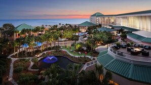 Un resort con piscina, palmeras y vista al océano al atardecer.