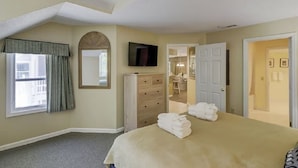 Un dormitorio con cama, cómoda, televisor y ventana con cortinas.