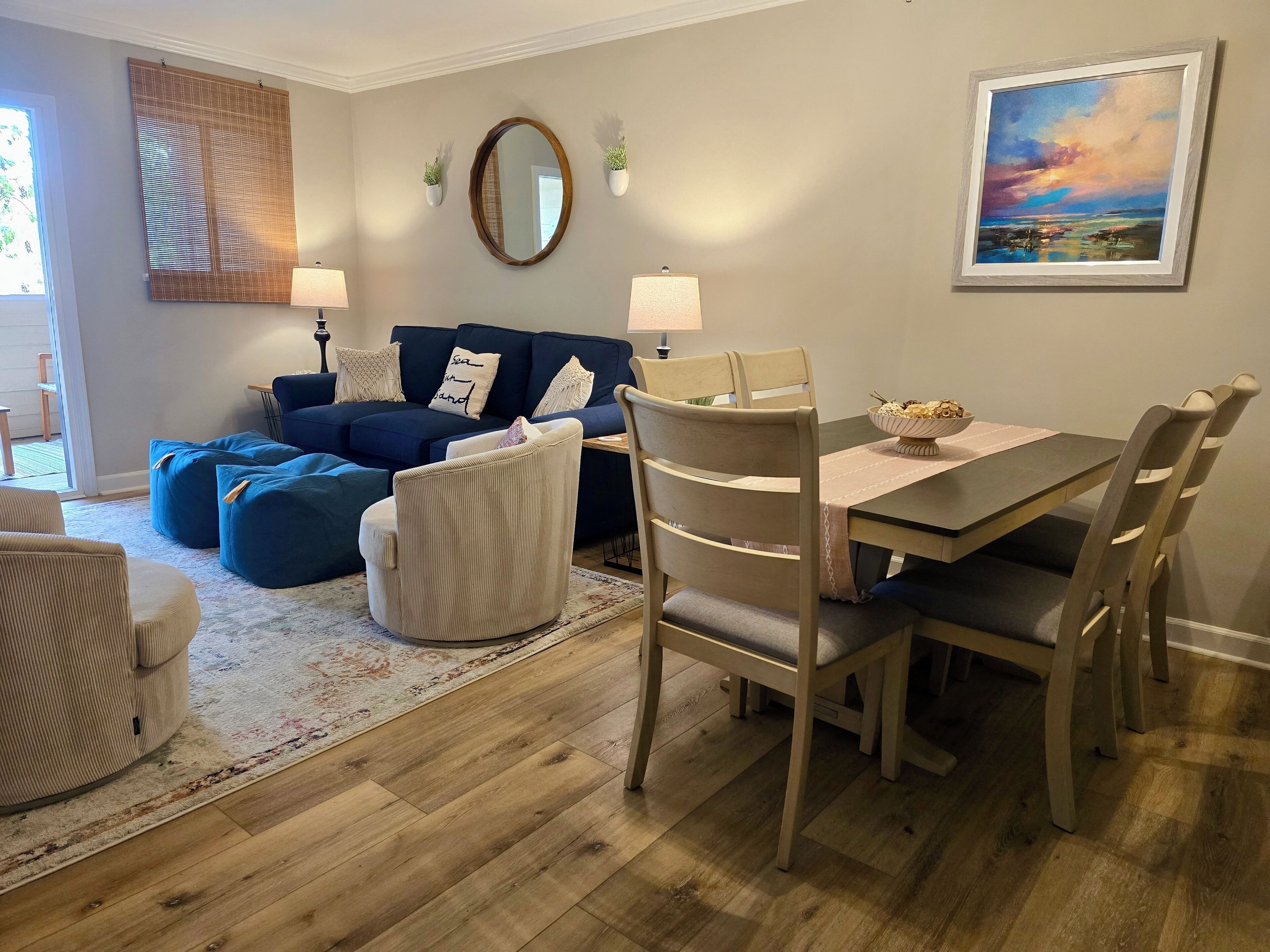 Een woonkamer met een blauwe bank, een eettafel met stoelen, een grote spiegel en een schilderij aan de muur.