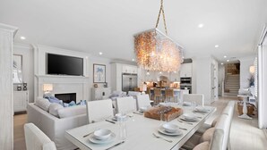 Una cocina moderna con armarios blancos, un televisor integrado y un comedor con una mesa blanca dispuesta para seis.