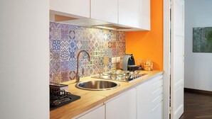 Een keuken met een kleurrijke tegelachtergrond, een roestvrijstalen spoelbak en witte kastjes.