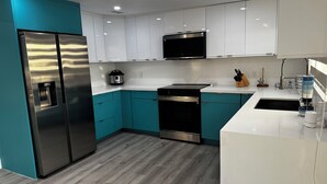 Una cocina moderna con armarios verde azulado y blancos, electrodomésticos de acero inoxidable y piso de madera.