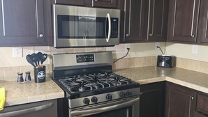 Uma cozinha com armários de madeira escura, micro-ondas de aço inoxidável, fogão a gás e forno embutido.