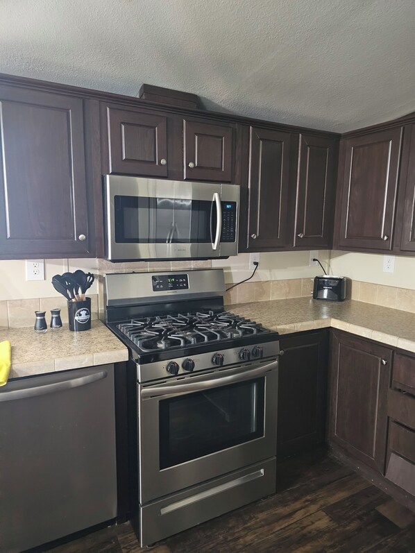 Una cocina con gabinetes de madera oscura, un microondas de acero inoxidable, una estufa a gas y un horno empotrado.