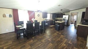 Uma cozinha espaçosa com piso de madeira escura, uma área de refeições com cadeiras e uma geladeira.