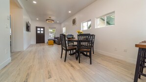 A spacious dining area with a wooden floor, a round table, and four chairs. There is a small yellow ottoman and a window with a view of the outside. - The Gunnison Bungalow in Downtown GJ! (Grand Junction)