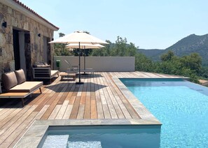 En træterrasse med pool, udendørs møbler og en bygning i sten.