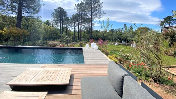 Eine Holzterrasse mit Pool, umgeben von Bäumen und einem Garten mit Blumen.