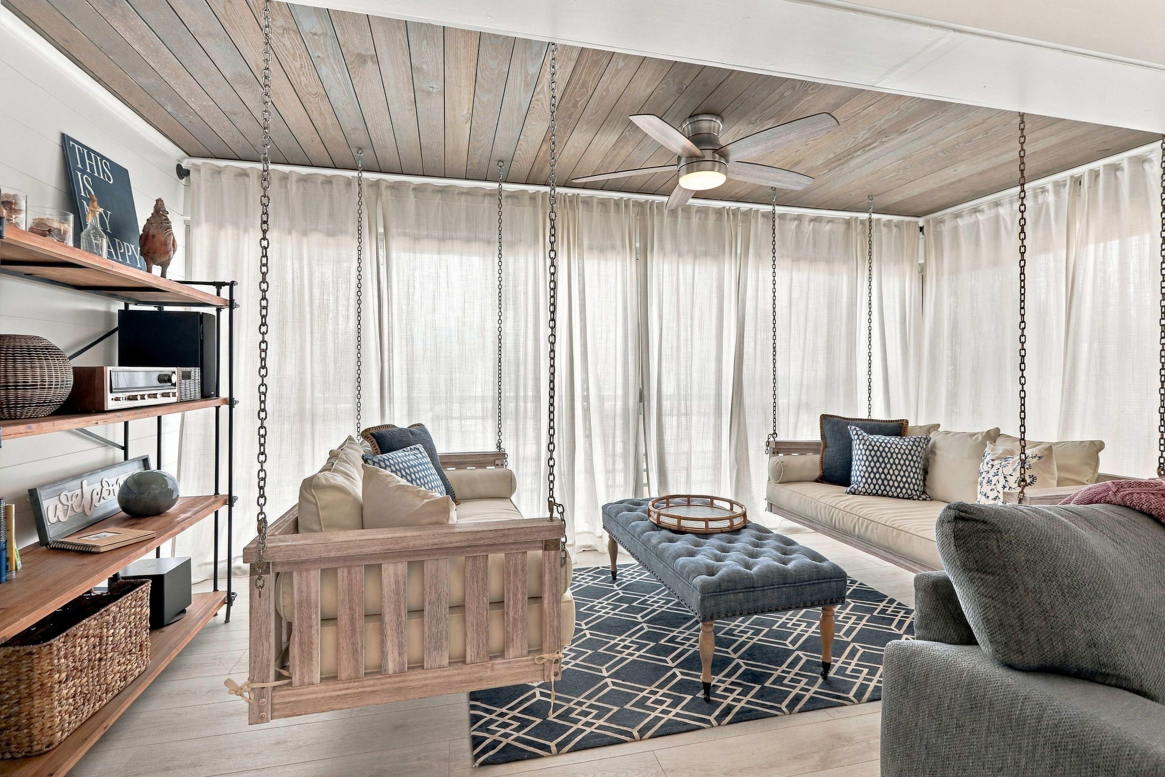 A living room with a wooden ceiling, a ceiling fan, a sofa, a loveseat, a wooden bench, and a patterned rug.