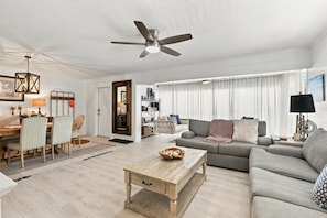 A living room with a ceiling fan, a dining area with chairs and a table, and a sofa with cushions. - Gulf-Side Paradise | Steps to the Beach | Pool (Fort Myers Beach)