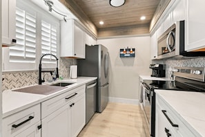 A modern kitchen with white cabinetry, a stainless steel refrigerator, a built-in oven, and a microwave. - Gulf-Side Paradise | Steps to the Beach | Pool (Fort Myers Beach)