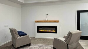 A modern living room with a fireplace, two armchairs, and a ceiling fan. - Halfmoon Hideaway-New Woodland Home Near Glacier (Columbia Falls)