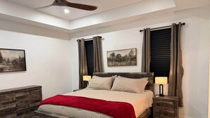 A bedroom with a wooden bed, two bedside tables, a ceiling fan, and two wall-mounted paintings. - Halfmoon Hideaway-New Woodland Home Near Glacier (Columbia Falls)