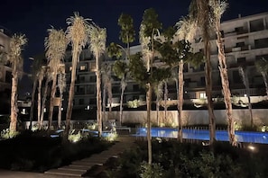 Ein Hotel bei Nacht mit mehreren Stockwerken, Palmen und einem Schwimmbad.
