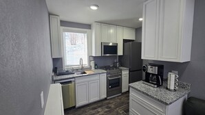 Una cocina moderna con armarios blancos, electrodomésticos de acero inoxidable, horno integrado y cafetera.