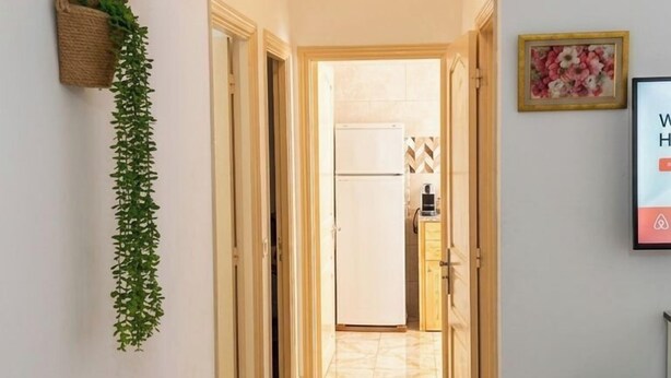 Um corredor com planta pendente, quadro emoldurado e chão de azulejos que leva a uma área de cozinha.