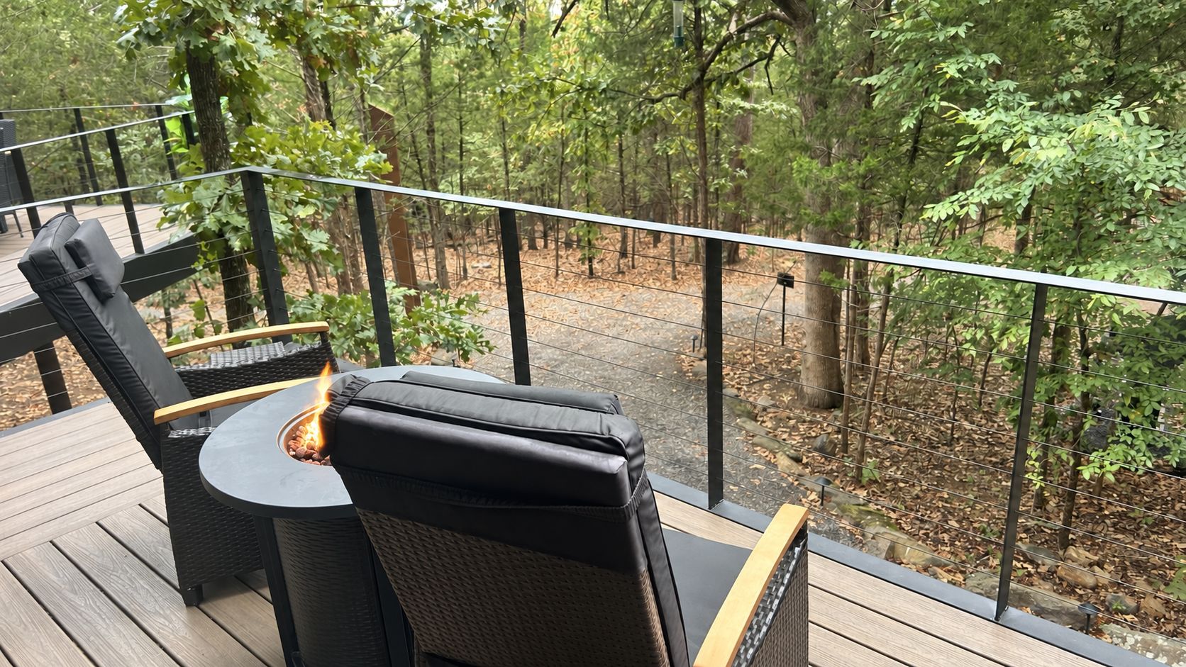 An outdoor deck with a fire pit table and chairs, surrounded by a wooden deck and a metal railing.