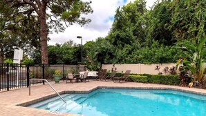 Une piscine rectangulaire avec un escalier en métal, entourée d’une terrasse en briques. On y trouve des chaises longues et une table avec des parasols.