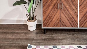 Un salon moderne avec un mur blanc, un grand téléviseur à écran plat fixé au-dessus d’un meuble en bois, une plante en pot et une petite table agrémentée d’objets décoratifs.