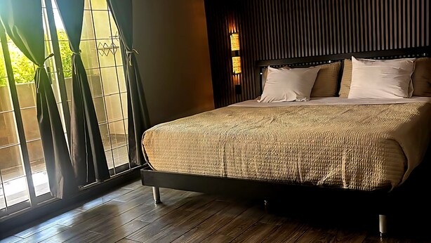 A bedroom with a large bed, wooden flooring, and a window with curtains. - Casa Jardines SLW, an ideal house for families or companies! (Saltillo)