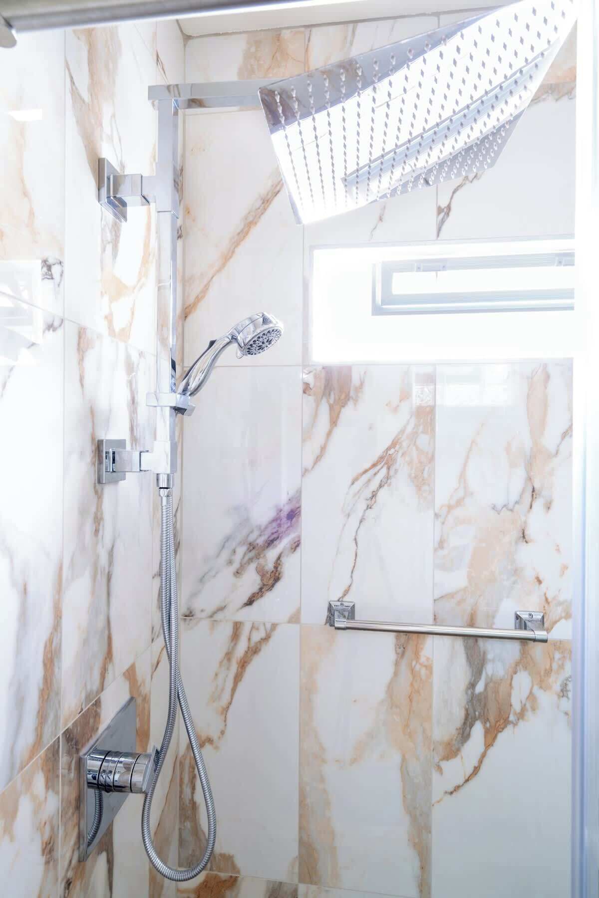 Un baño moderno con ducha, azulejos de mármol y un perchero para toallas.