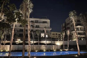 A multi-story hotel with a pool area, palm trees, and a night sky. - Luxury Studio Pool View At Sodic Villette (Cairo Governorate)