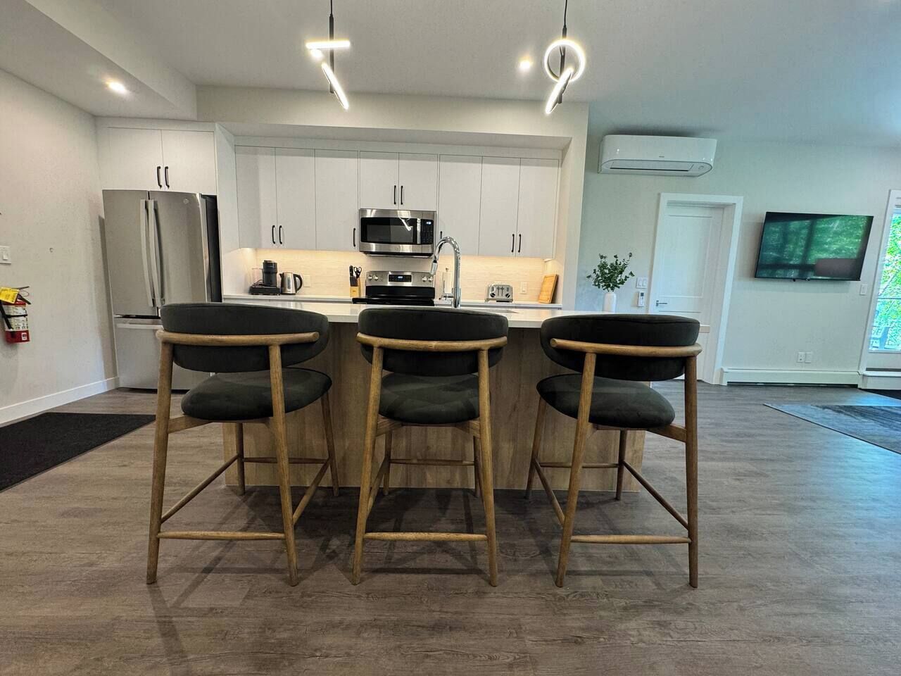 A modern kitchen with a central island, bar stools, and a flat-screen TV mounted on the wall.