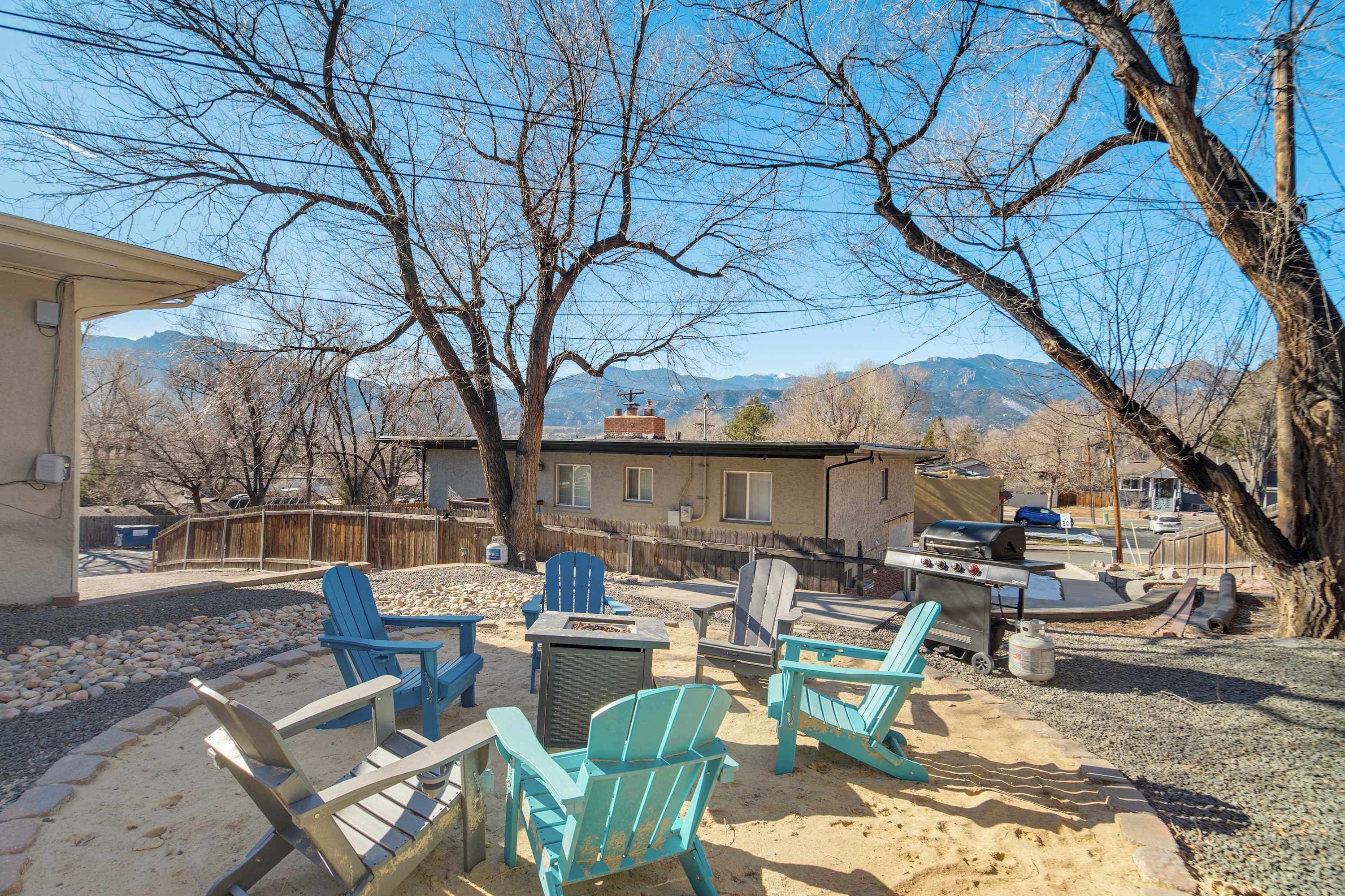 A backyard with Adirondack chairs, a grill, and a view of mountains.