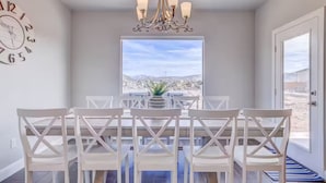 A dining area with a table and chairs, a chandelier, a clock, and a view of the desert through a large window. - Premium Family Escape: Heated Pool, Private Hot Tub, Fire Pit & Games (Hurricane)