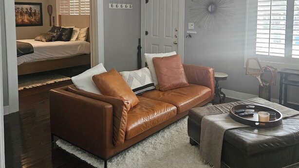 Ein Wohnzimmer mit einem braunen Ledersofa, einem weißen, flauschigen Teppich und einem Couchtisch mit einer Ablage.