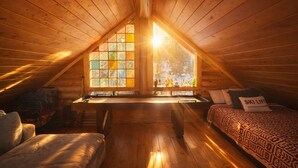 Une chambre mansardée chaleureuse, avec un plafond en pente, une grande fenêtre à carreaux, un bureau, un lit avec une literie à motifs et un coussin orné de l’inscription « SKI LIFT ».