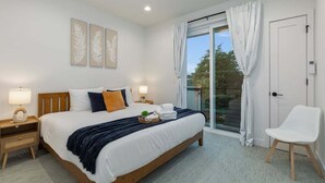 Ein Schlafzimmer mit einem großen Bett, zwei Nachttischen, einem weißen Stuhl und einem Balkon mit Vorhängen.