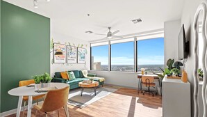 Un salon moderne avec un mur d’accent vert, un canapé, une table à manger avec des chaises, un ventilateur de plafond et une grande fenêtre donnant sur la ville.