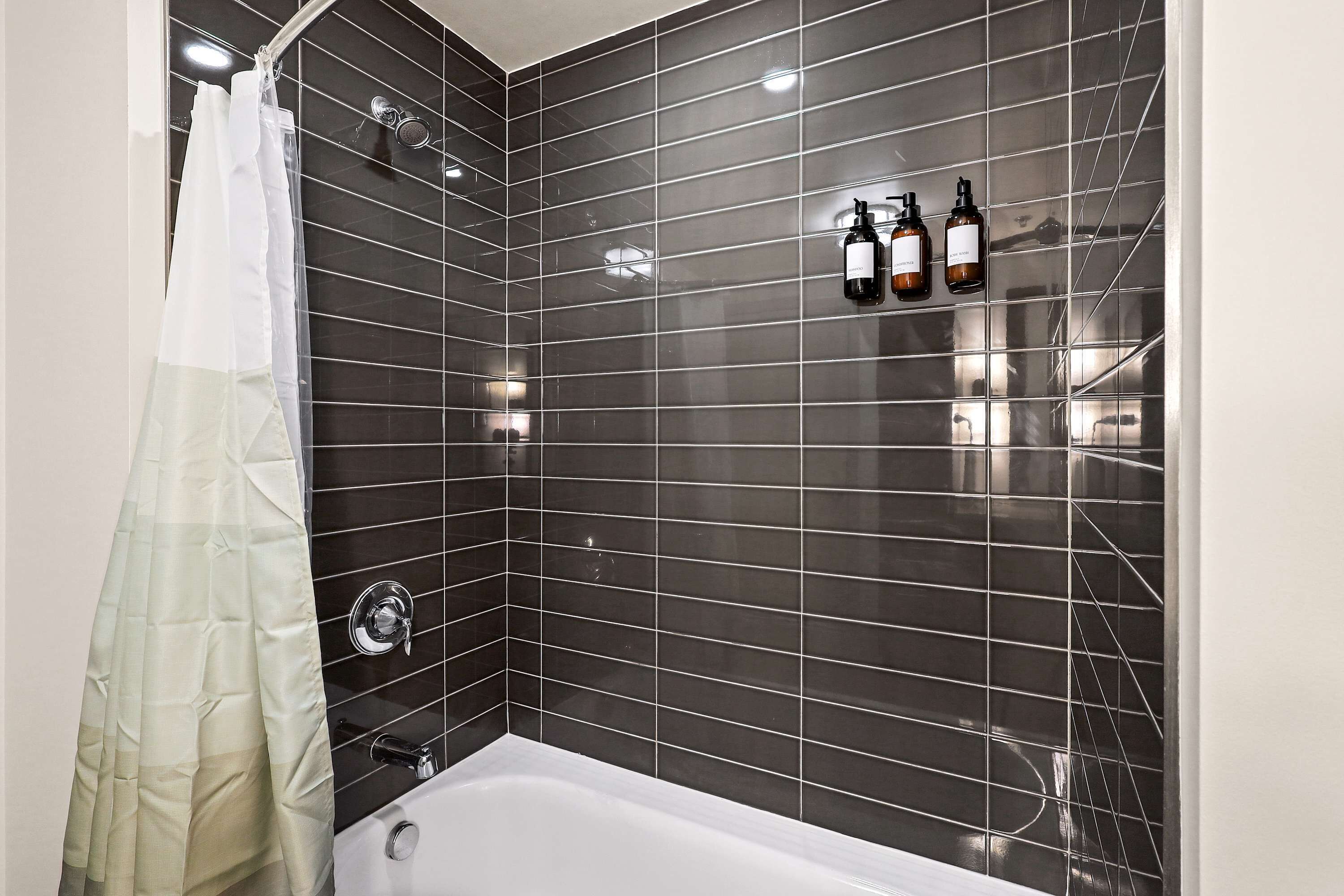 A modern bathroom with dark tiled walls, a white bathtub, and a shower curtain.