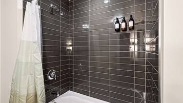 A modern bathroom with dark tiled walls, a white bathtub, and a shower curtain.