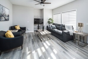 A modern living room with a black leather sofa, a wooden coffee table, and a grey couch.