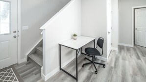 Un espacio de oficina moderno con un escritorio blanco y una silla de oficina negra, una escalera y una pequeña planta en maceta.