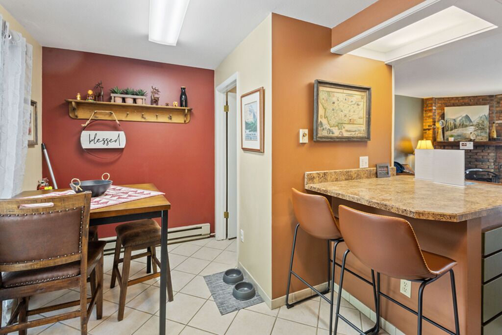 Cocina compacta con zona de comedor, que destaca por una pared roja, una mesa de madera y un pequeño mostrador con taburetes.