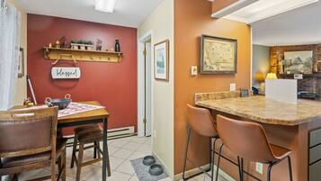 Cocina compacta con zona de comedor, que destaca por una pared roja, una mesa de madera y un pequeño mostrador con taburetes.