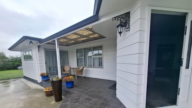 Un patio couvert aménagé avec des sièges, des plantes en pot et une porte donnant sur l’intérieur.