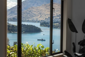 A view through a window of a lake with a boat, mountains, and a small island. - Fabulous Home with Great Views (Queenstown)
