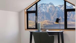 Habitació amb escriptori i cadira orientades a una finestra gran amb vista a la muntanya.