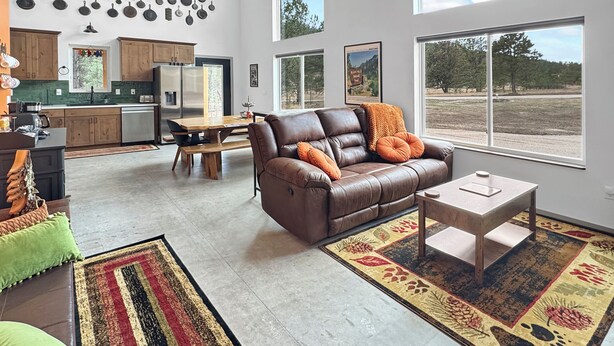 A spacious living area with a leather sofa, a dining table, and a kitchen in the background. - New Black Hills Home Next to Wind Cave National Park (Custer)